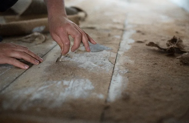 Person entfernt Kleber von Holzdielen